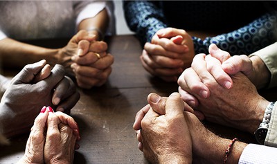 Group of people with interlocked fingers praying together