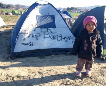 A child stands outside a tent at a refugee camp on the Macedonia-Greece Border.