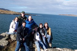 A group of people sitting on a cliff near a body of water.