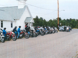 A group of people on motorcycles in a line in front of a church.