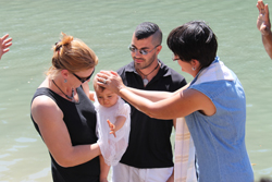Several people baptize a baby in a river.
