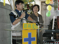 Choon and Yen Hee Lim standing together at a lecturn with yellow signs in Chinese as Choon speaks into a microphone.