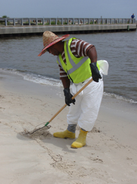 A man in a bright yellow-green vest cleaning up oil from a beach.