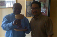 Two men standing side by side, smiling. One is holding a chalice and paten