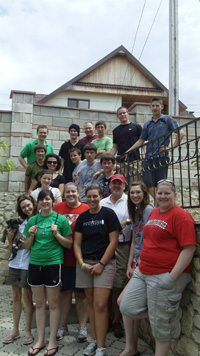 A group of volunteers standing beside a stone wall with a steel fence, on ground and stair level.