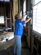 A woman using an electric nail gun to remove metal bars from a window.