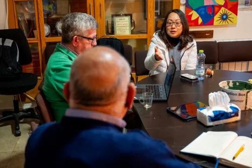 A woman speaks and gestures across the table to an unseen man during a meeting.