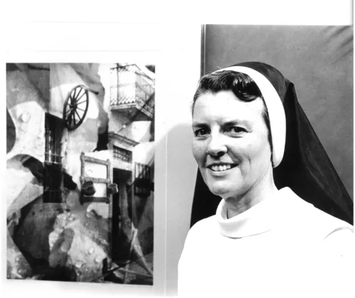 A woman wearing a nun's habit stands to the right of a piece of her art, on display. She is an artist-in-residence, and a photographer, AND a nun.