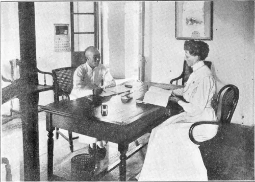 Dr. Mary Fulton sits at a desk with a textbook open in front of her. Across from her, a Chinese man listens and advises her in her translations.