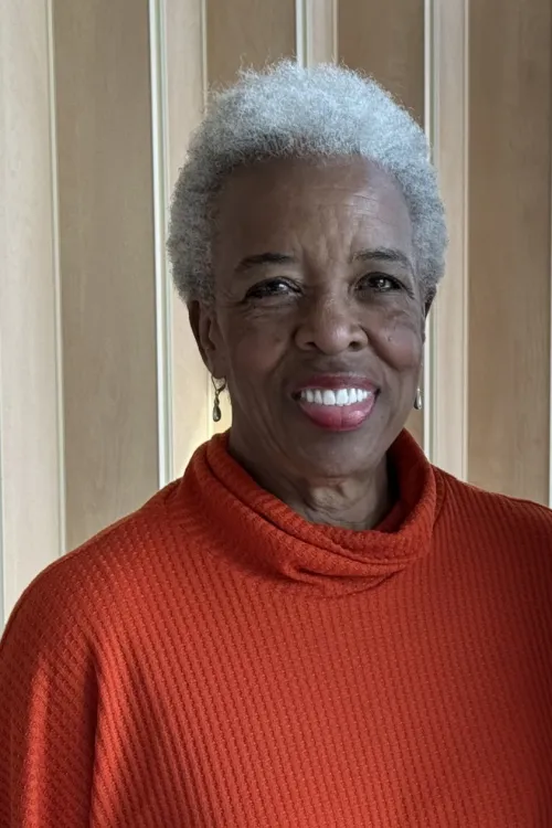 A woman in a red turtleneck photographed against a multilayered background.