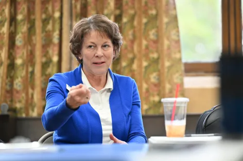 A woman in a blue jacket makes a point at a table in a brightly lit room