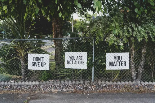 Signs with uplifting statements near a fence and lush vegetation 