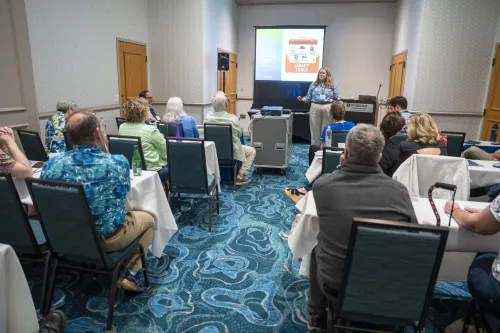 A woman leads a conversation with multimedia projections in a small hotel meeting room.