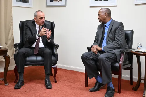 Two men sitting in chairs speak to one another.