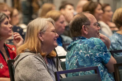 People smile in an audience listening to an unseen speaker