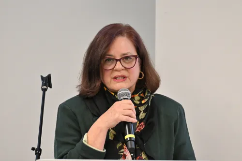 A close-up photo of a woman speaking at a meeting using a handheld microphone.