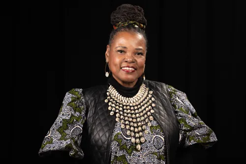 A formal portrait of a woman in an elaborate black, gray and gold dress against a black backdrop.