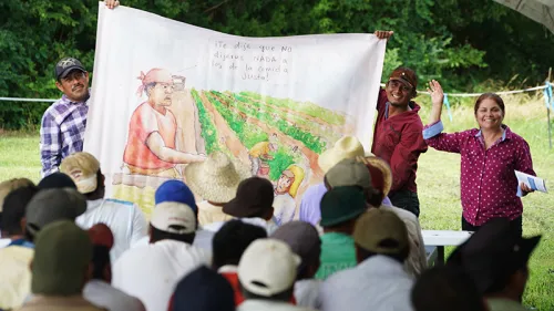 Three people holding up a drawing of workers in the field.