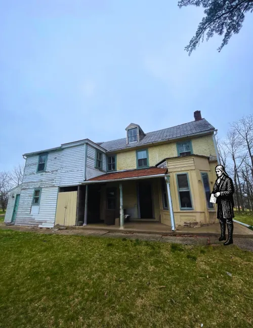 A photo of the William Tennent House taken in early April 2026; cartoon image of William Tennent to the right of the house.