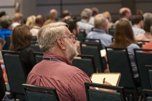 A person in an audience listens to an unseen speaker.