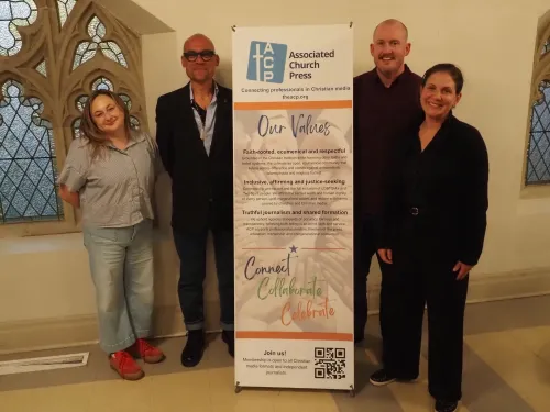 Four people stand around a banner at the Associated Church Press convention in Toronto.