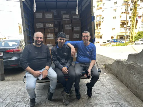 Men seated at the back of an open truck filled with boxes