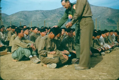 Harold Voelkel rests his palm atop a Korean POWs head as he prays over him.