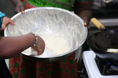 hand stirring a spoon inside bowl next to a pan frying dough