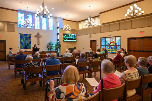 person addressing worshippers inside sanctuary, with windows at back and right side showing