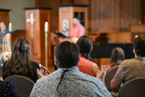 worshippers with back to camera foregrounded with persons leading service in background