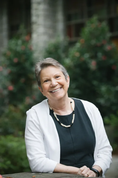A woman smiling joyfully in an outdoor setting while wearing a white jacket and black blouse.