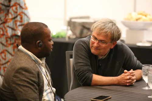 two men sitting at a table and talking to one another