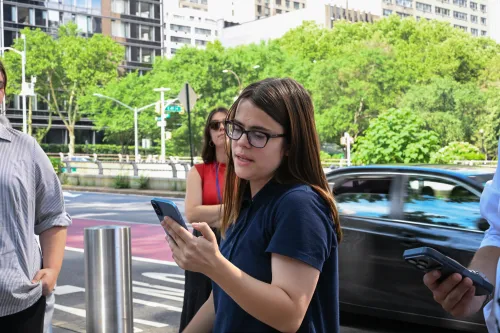 A young woman on a city sidewalk reads a prayer from her cell phone