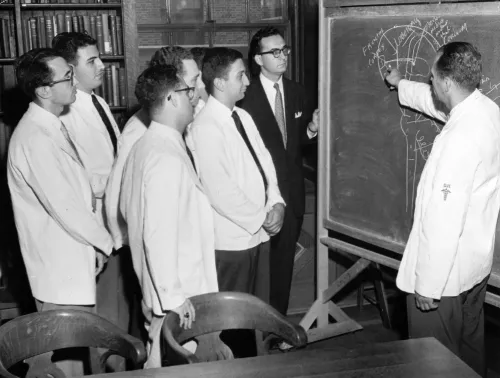 A group of men look on as a man draws on a chalkboard.