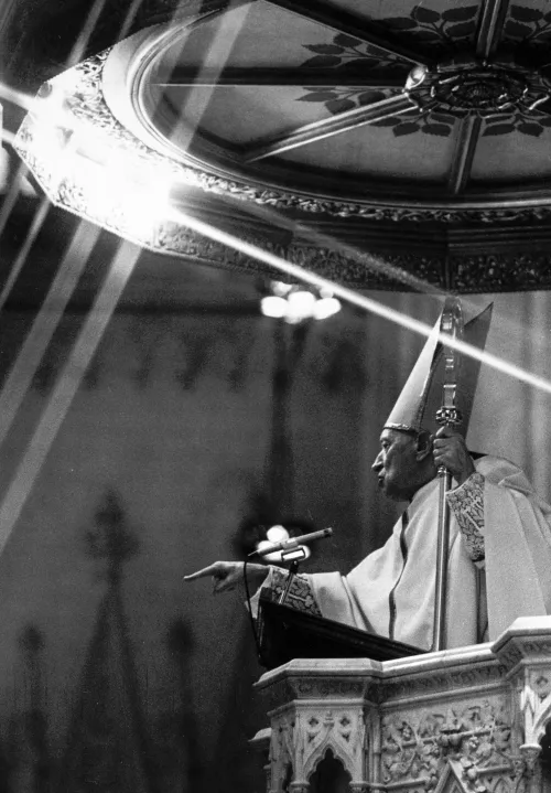 Cardinal Mindszenty in 1974, three years after his exile from Hungary and just a year before his death, preaching from the pulpit of a church. A glaring light shines above him to the left of the frame.