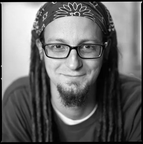 A man with glasses and a bandana looks directly into the camera in a black-and-white photograph