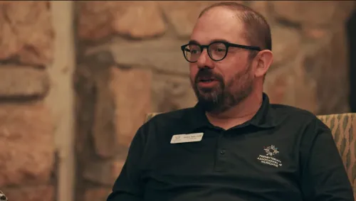 A man in a polo shirt speaks in front of a stone wall