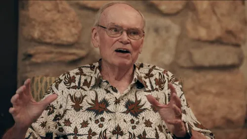 A man in a snazzy casual shirt appears to be in conversation in front of a stone wall.