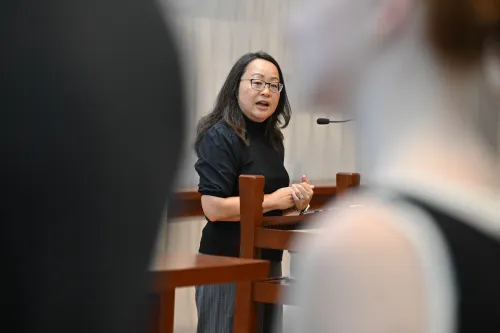 A woman in a black tops stands and speaks to a crowd