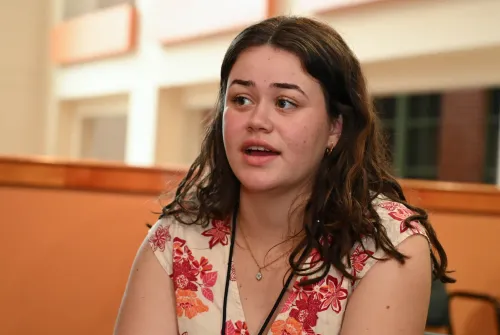 A young woman in a floral dress speaks
