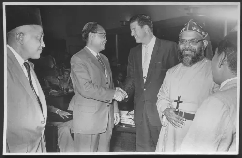 Four men chatting, shaking hands, conversing-black and white photo dating to 1957.
