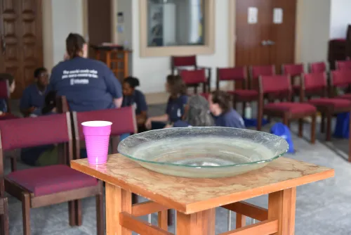 Students in background as pink Solo cup holds holy water near baptismal font in Harrington Chapel at Columbia Theological Seminary during UKirk retreat.