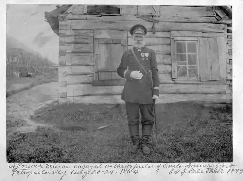 A man wearing an army uniform stands outside a clapboard house, one arm at his waist, the other leaning on a cane.