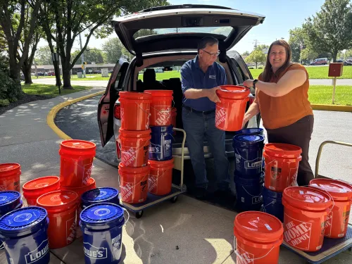 A man and a woman posing with cleanup buckets behind a van