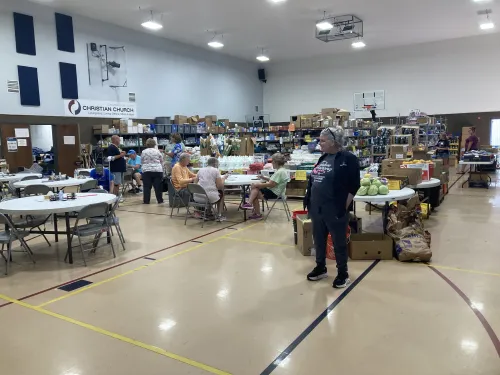 People sit at tables and stand around in a large room filled with supplies