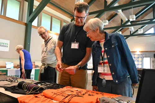 A man shows a woman a piece of jewelry from a table of jewelry in a large room.