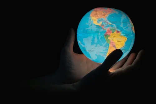 Hand in dark holds up an illuminated sphere of the world