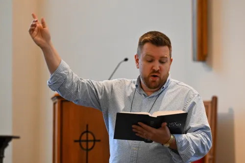 A man holding a hymnal holds his arm up as he leads worship.