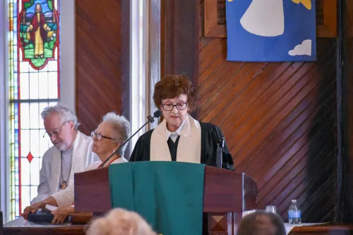 A woman in a clergy stole stands at a podium and looks down