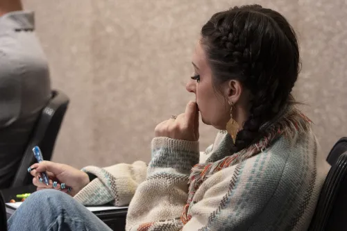 A woman takes notes while listening to an unseen speaker.